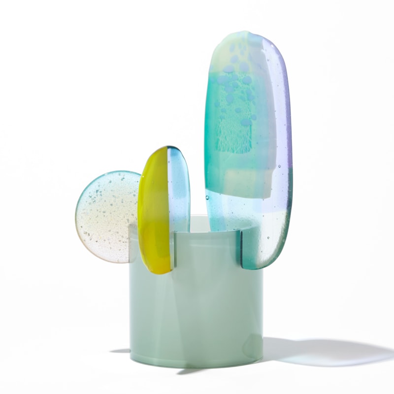 short opaque celadon cylinder with three rounded petals overlapping and perched on the top rim in lilac jade lime green and clear hand made from blown and fused glass